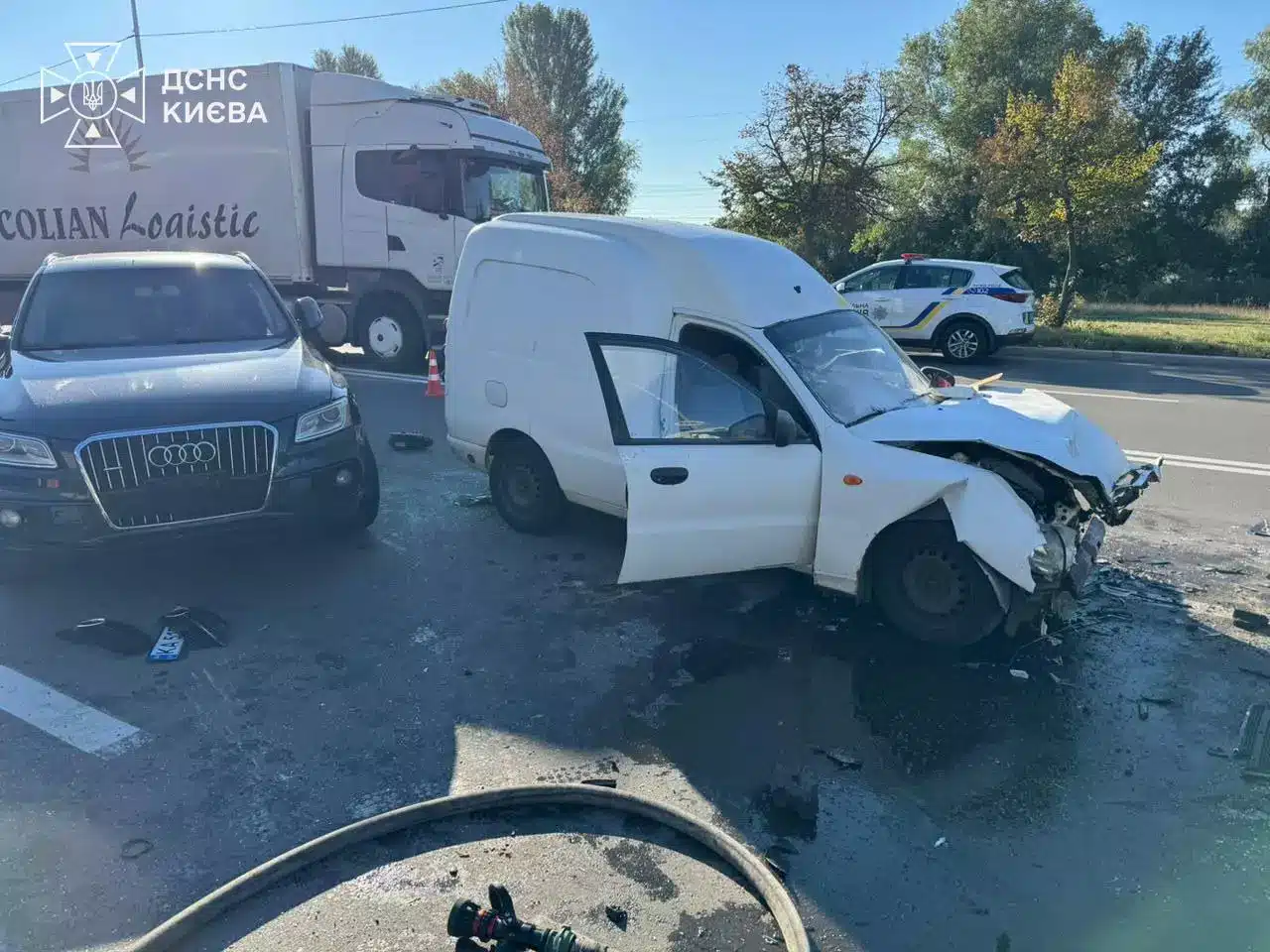 Білий мікроавтобус з пошкодженою передньою частиною, чорний Audi та вантажівка на місці дорожної аварії на шосе