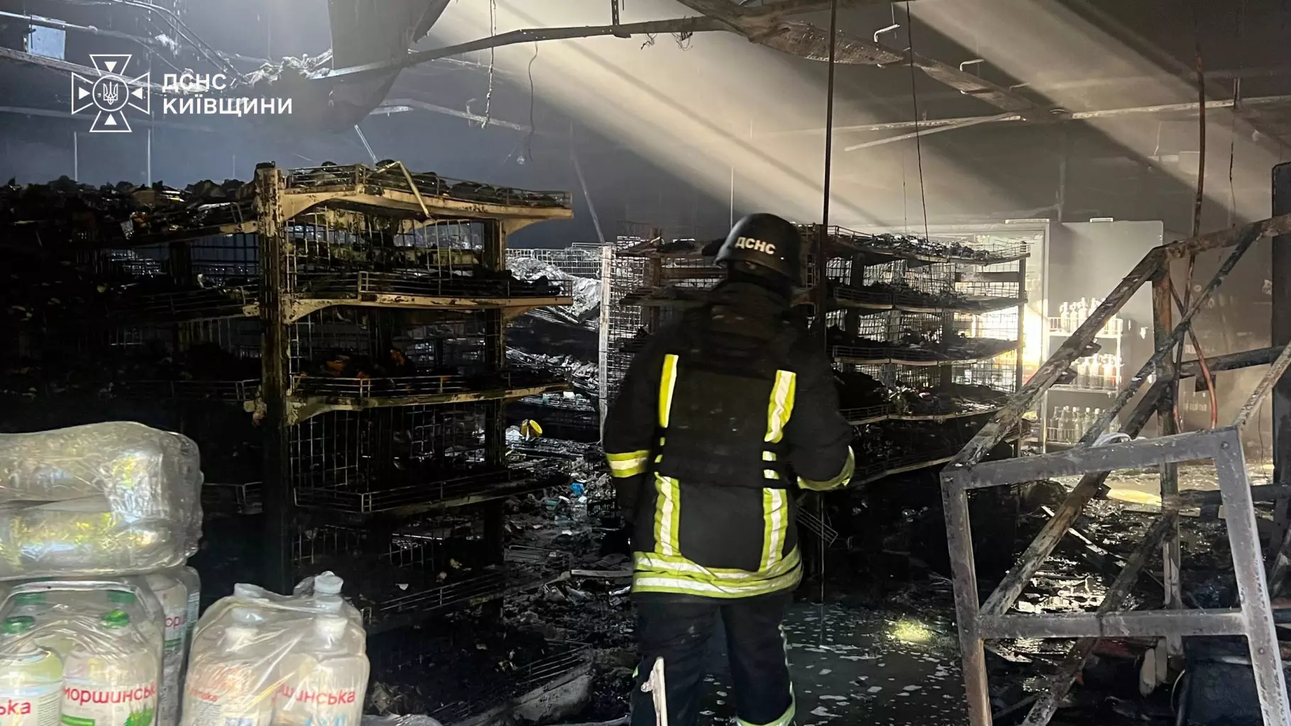 Рятувальник у спеціальному екіпірунні та рятувальниця працюють всередині супермаркету серед обгорілих залишків товарів та