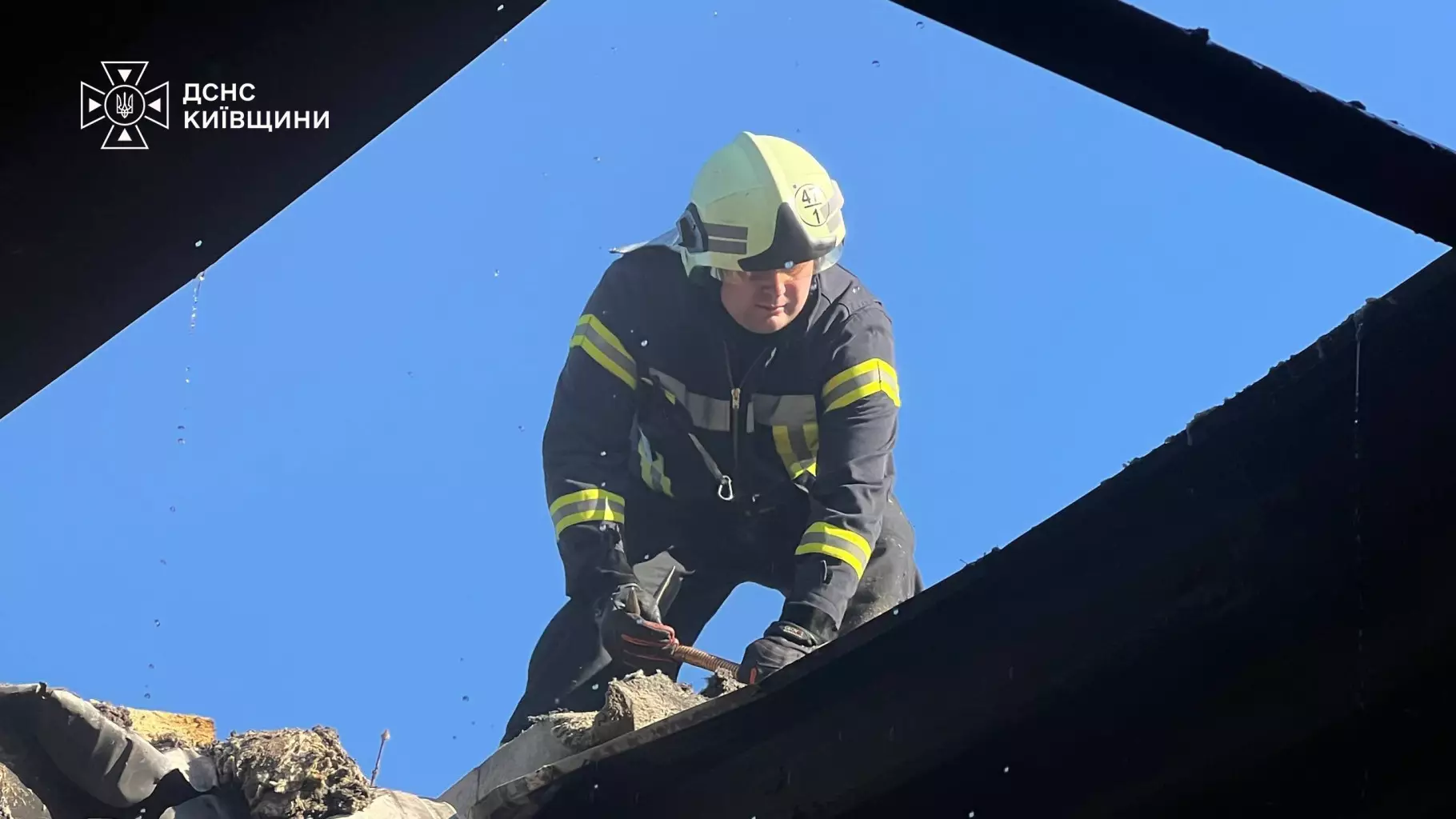 Рятувальник у захисній формі розбирає обгорілі конструкції даху супермаркету під час ліквідації наслідків атаки