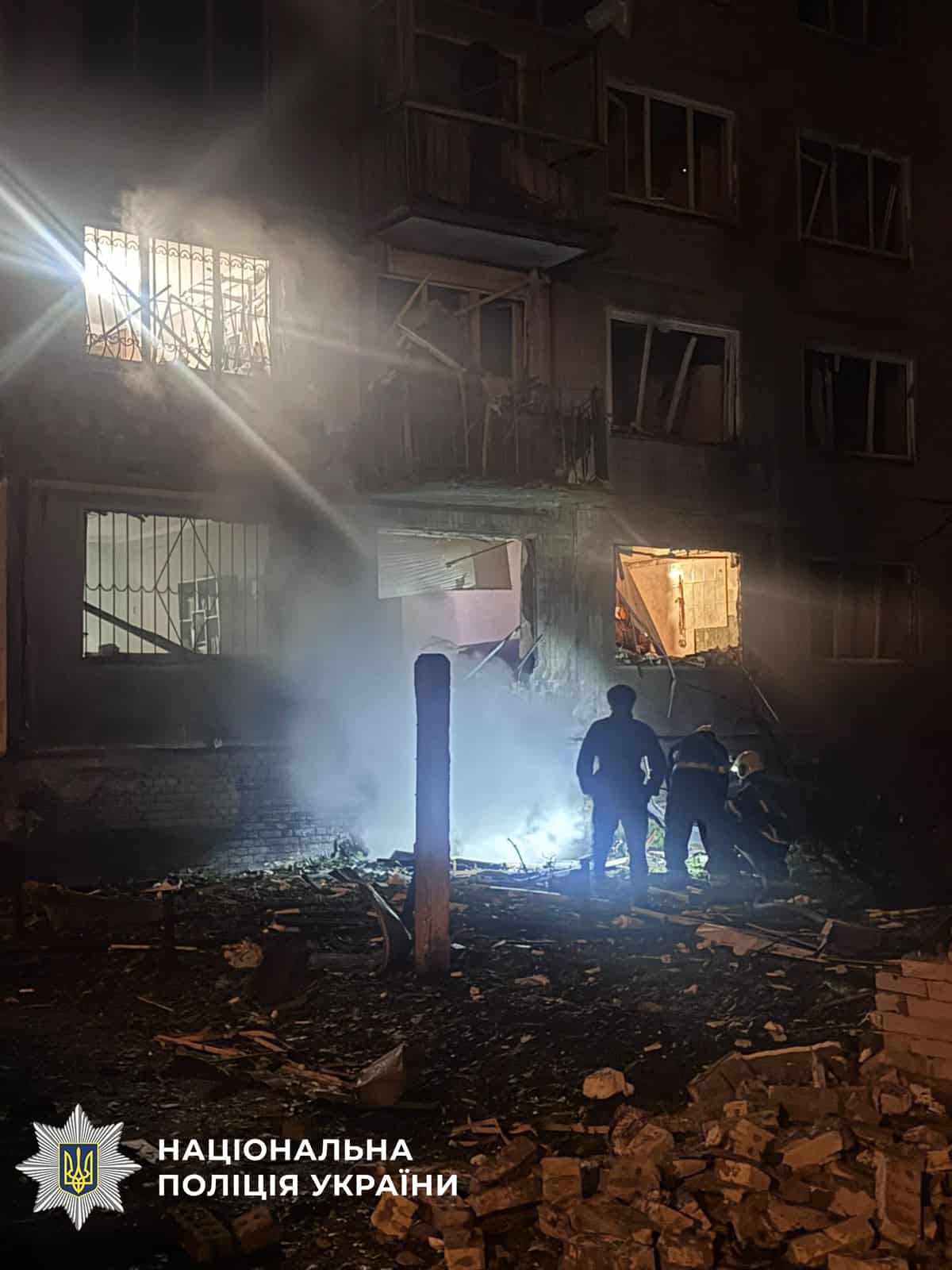 Поліцейські та рятувальники працюють на завалах у світлі лампи серед розвалин пошкодженої будівлі