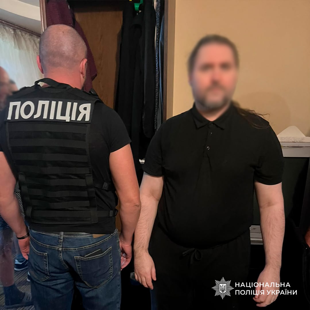 Поліцейський розмовляє з чоловіком у квартирі під час проведення слідчих дій у справі про незаконне бронювання від призову