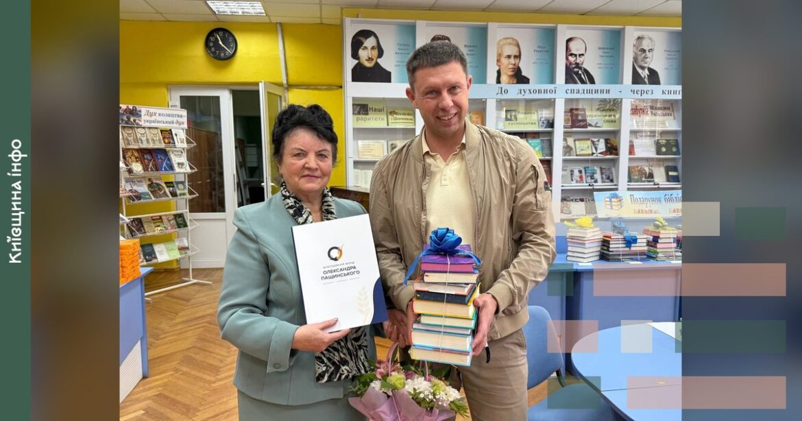 Чоловік і жінка тримають стопку книжок та документ у бібліотеці під час передачі дару до Дня бібліотек