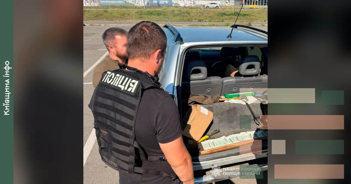 Поліцейський при автомобілі демонструє вилучені під час обшуку грошові кошти та документи у справі про побори з лісництв