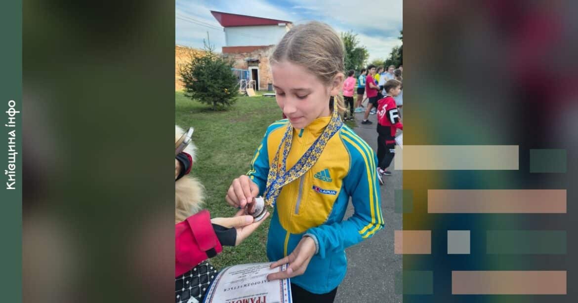 Дівчина у жовто-синій спортивній куртці з медалями розглядає сертифікат на спортивному заході