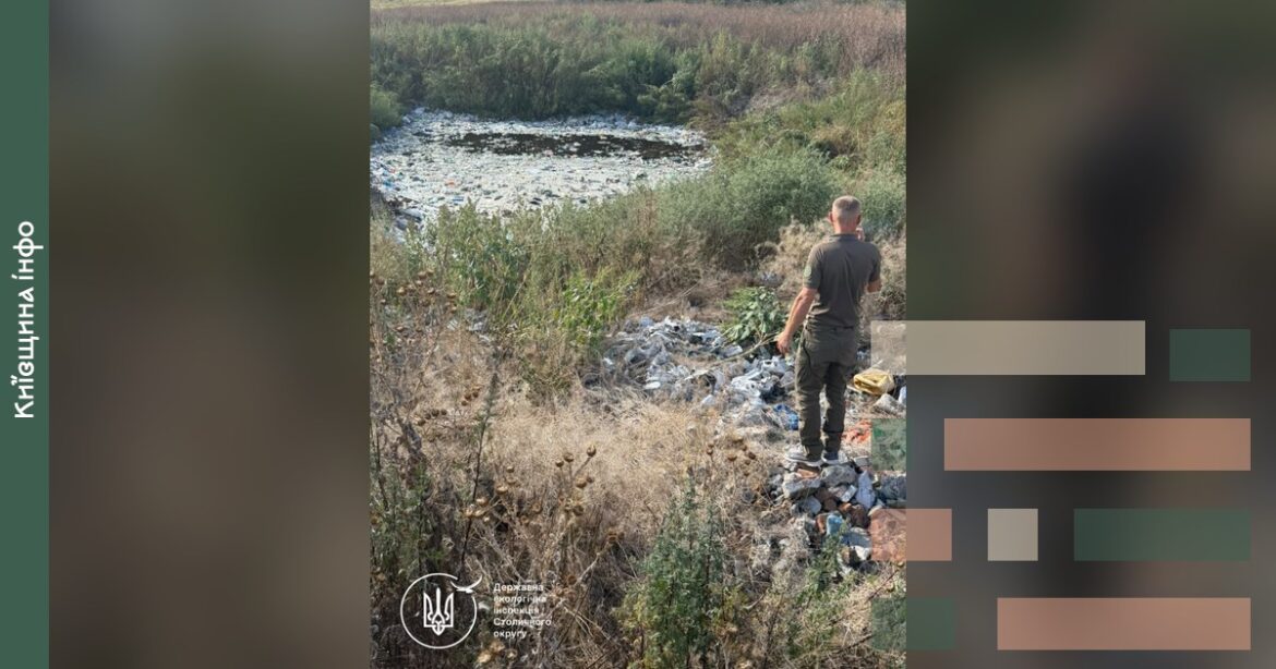 Інспектор у чорній футболці стоїть на край берега річки, засипаної сміттям, на Білоцерківщині