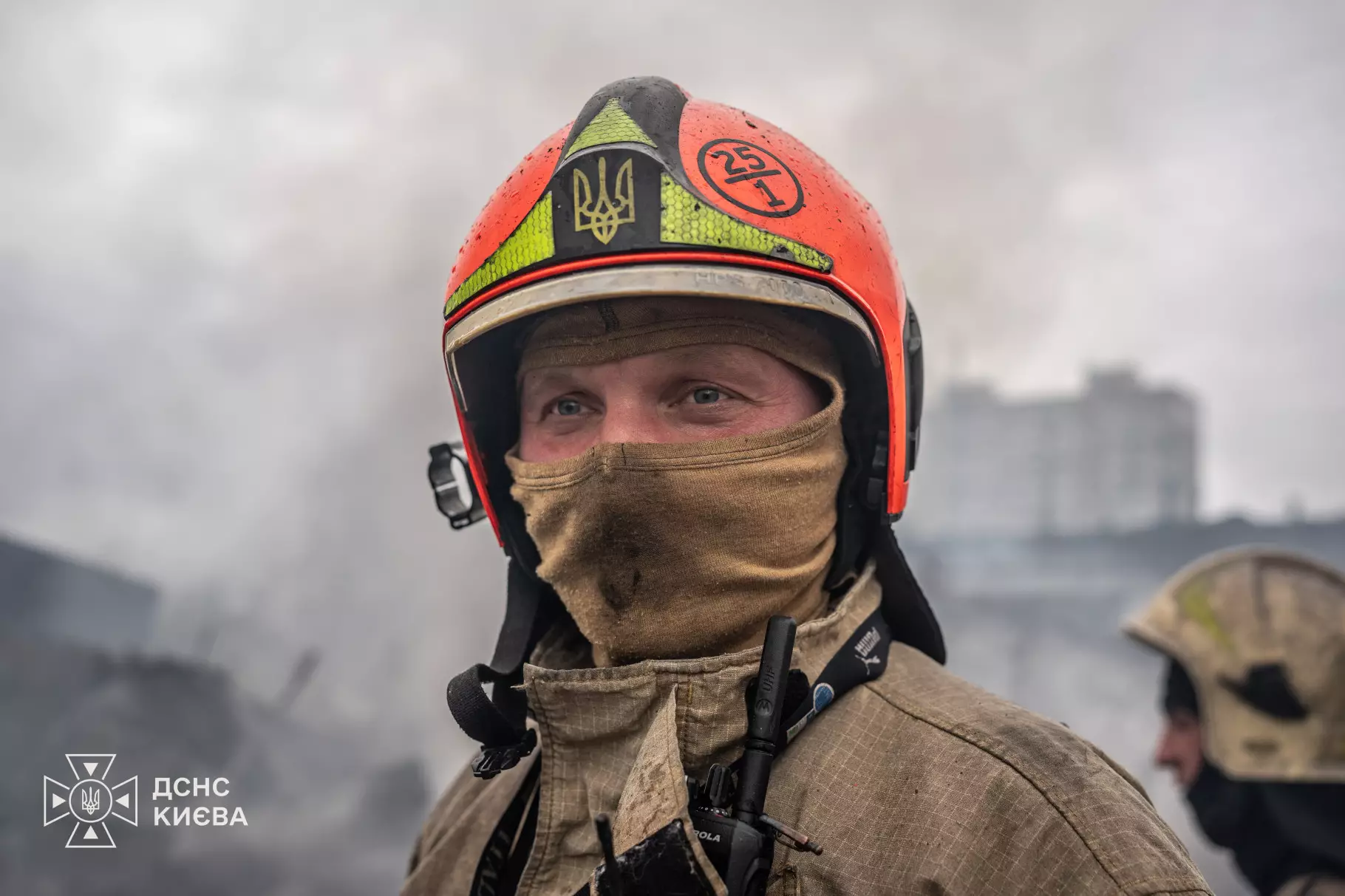 Портрет рятувальника у червоно-жовтому шоломі з українським гербом на тлі міста