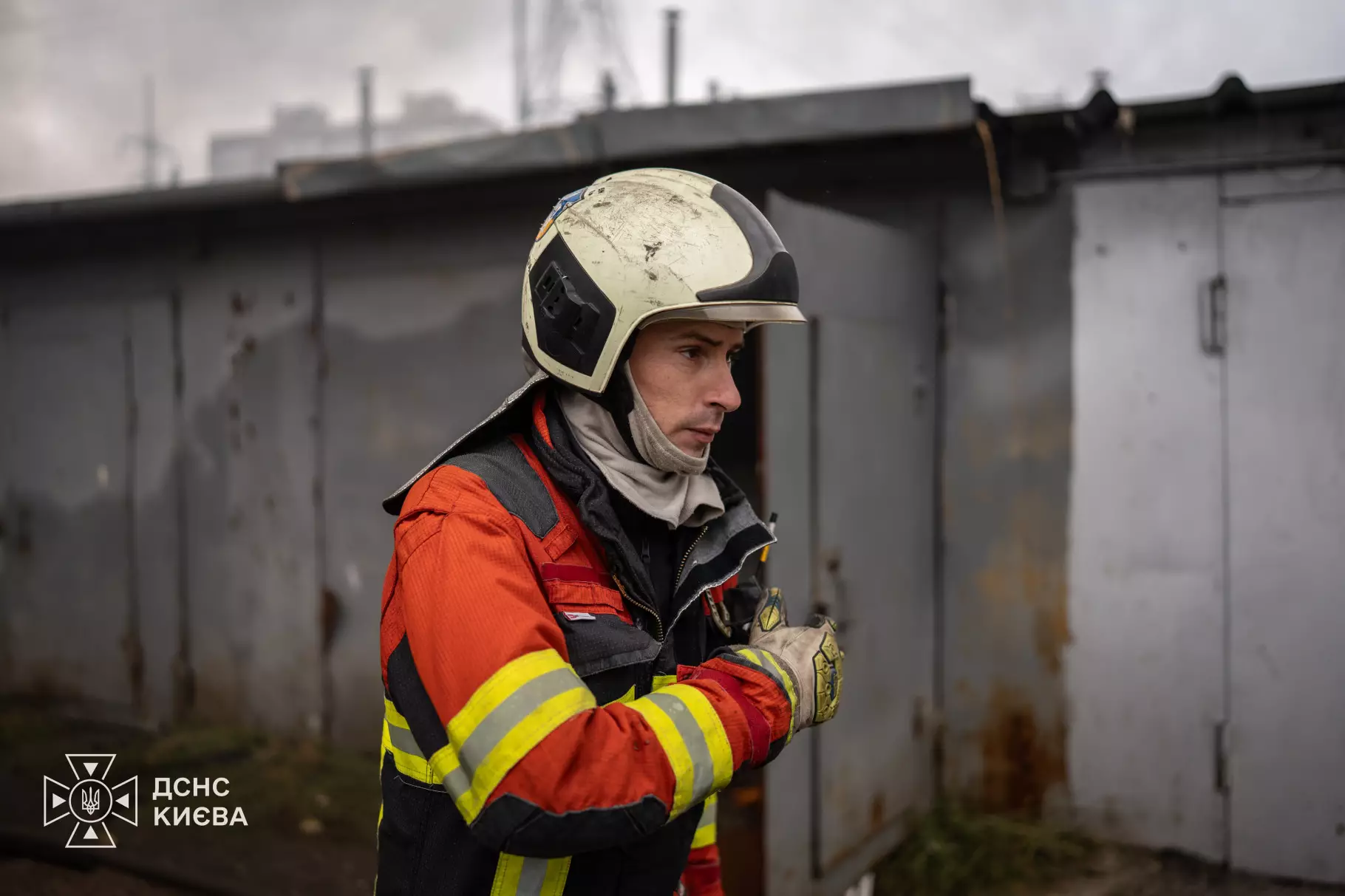 Рятувальник у оранжево-чорному костюмі біля гаражних боксів на місці обстрілу