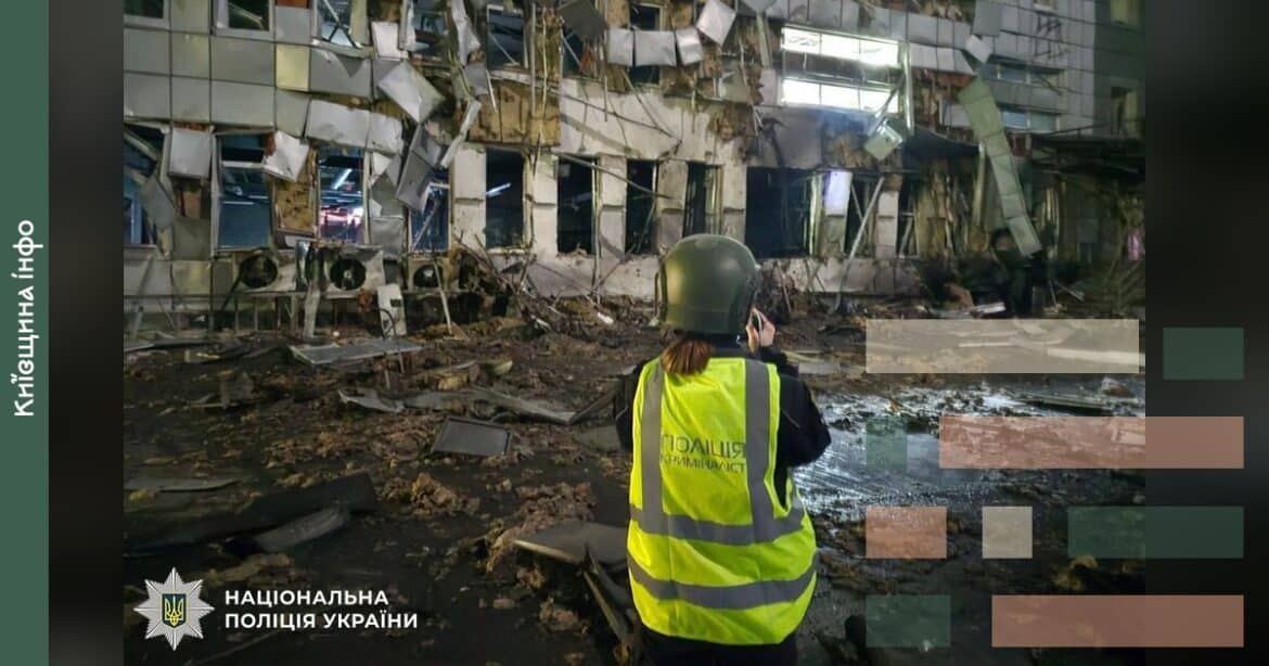 Поліцейський у жовтому жилеті документує пошкодження багатоповерхового будинку з вибитими вікнами та зруйнованим фасадом