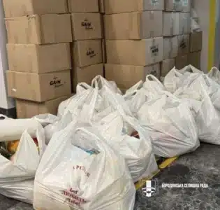Картонні коробки та білі пакунки з продуктами розташовані у приміщенні для розповсюдження родинам