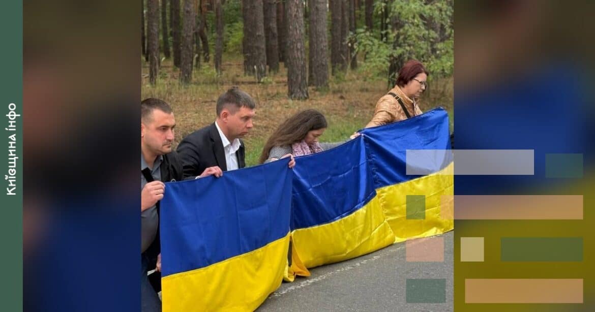 Люди тримають синьо-жовтий прапор України під час церемонії прощання з захисником