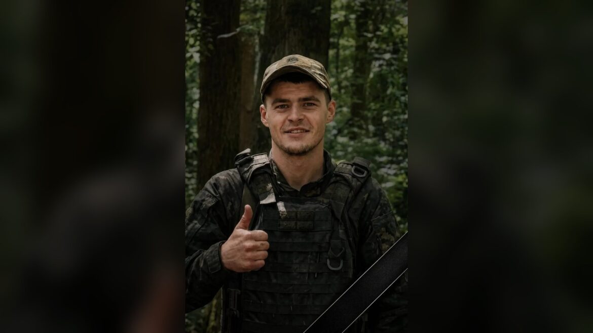 Чоловік у військовому спорядженні та кепці дає знак «палець вгору» на фоні лісу