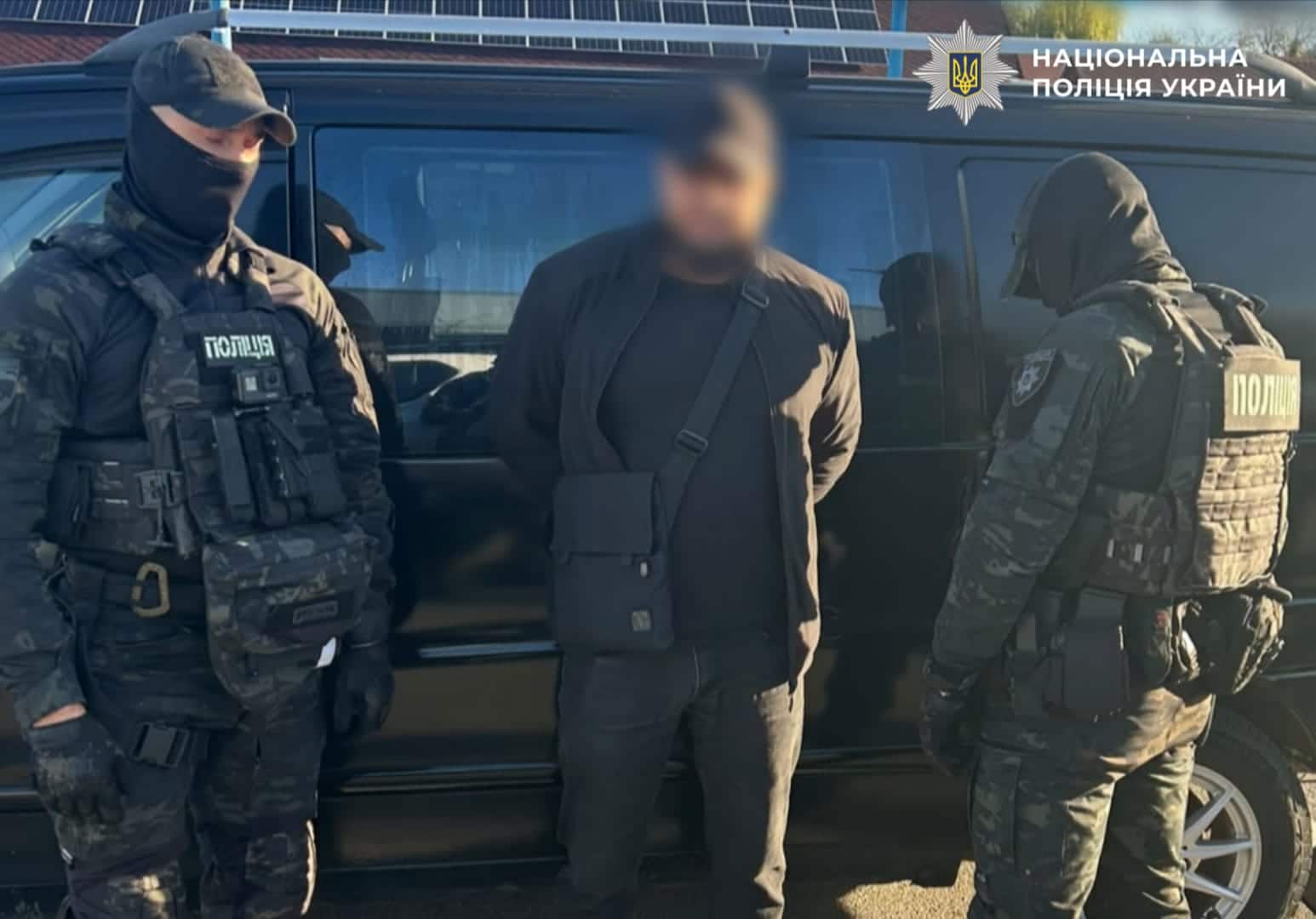 Поліцейські конвоюють затриманого чоловіка в чорному костюмі до служебного автобуса