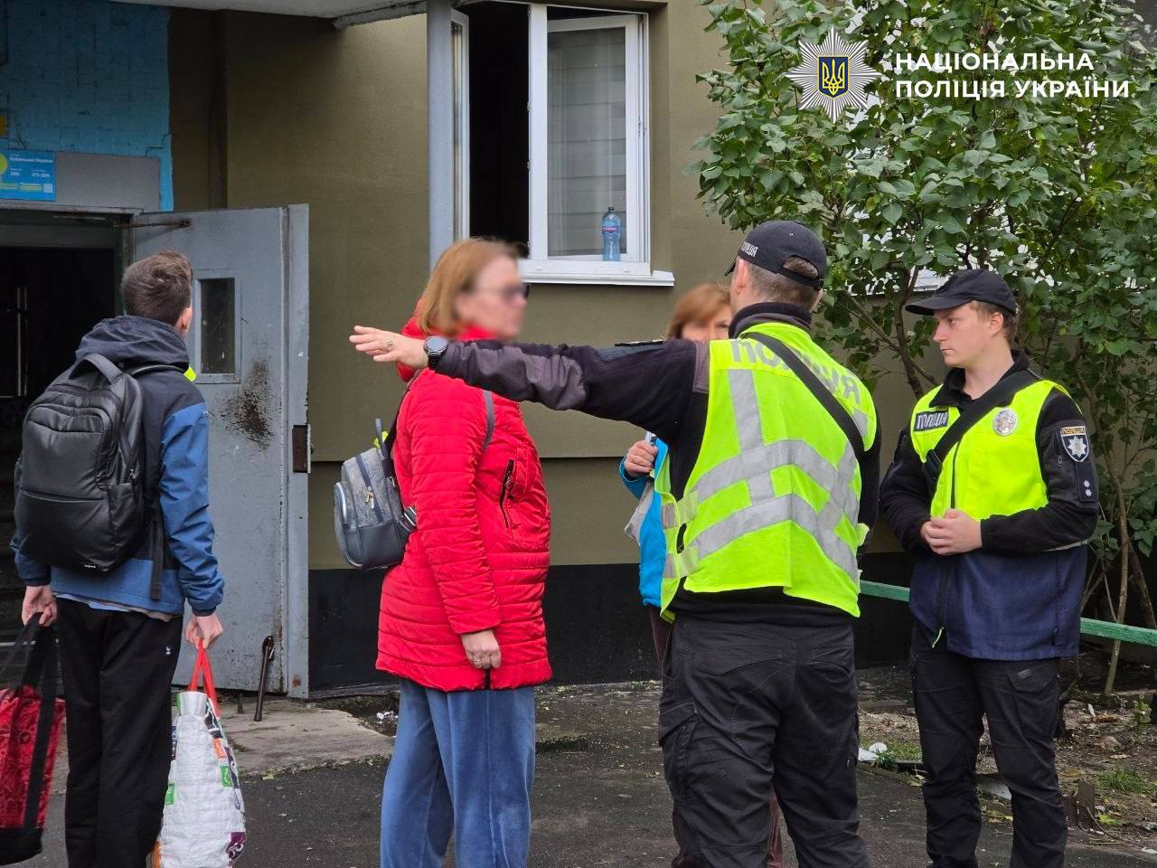 Поліцейські спілкуються з евакуйованою жінкою біля входу до житлового будинку