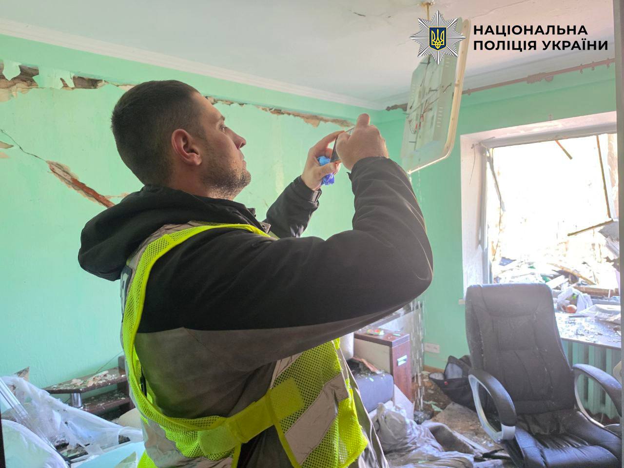 Поліцейський фотографує пошкодження стелі та стін у кімнаті зруйнованого житлового будинку