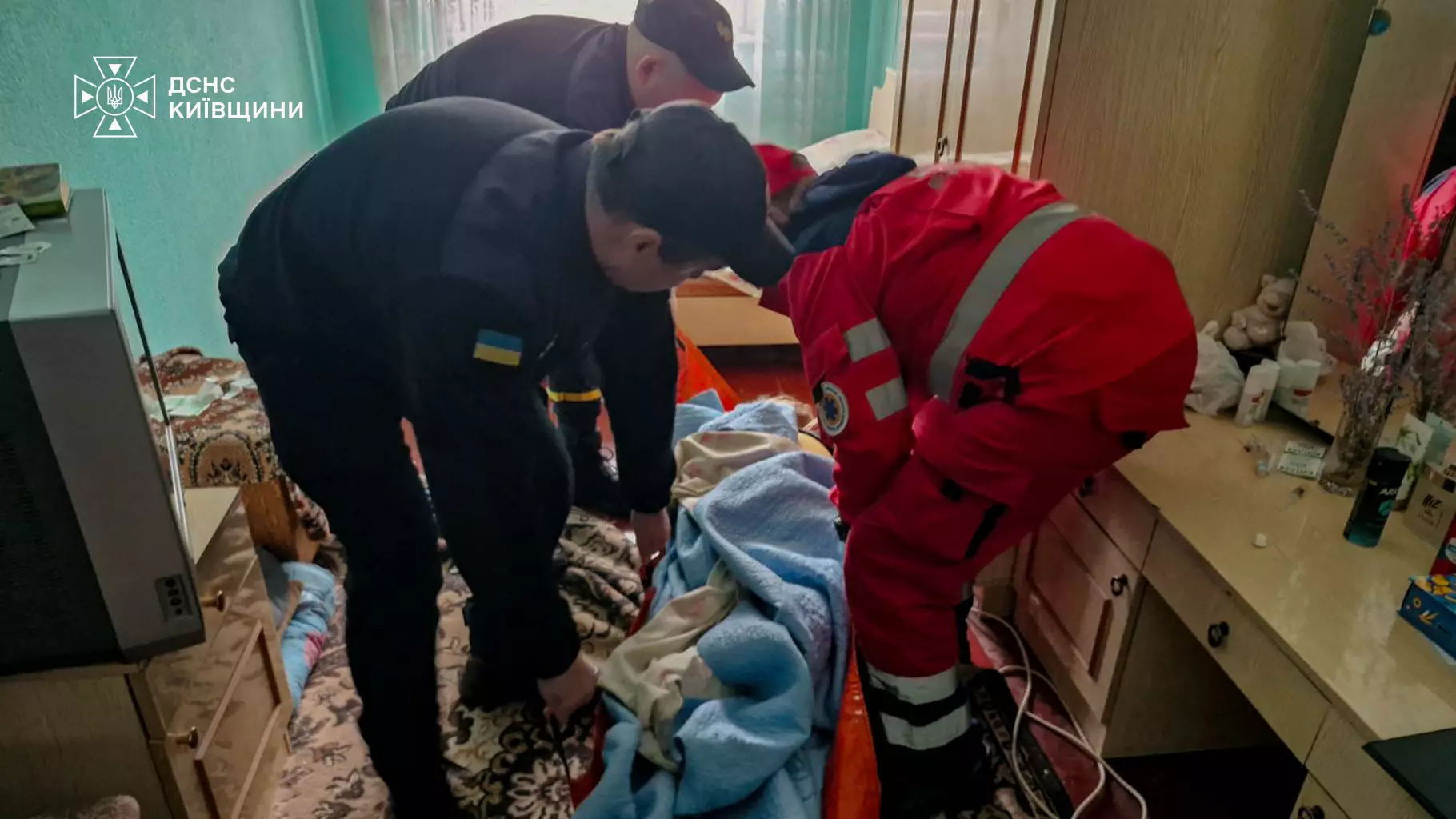Поліцейські та рятувальник у червоному костюмі допомагають чоловікові встати з підлоги квартири на вулиці Павліченко у Білій