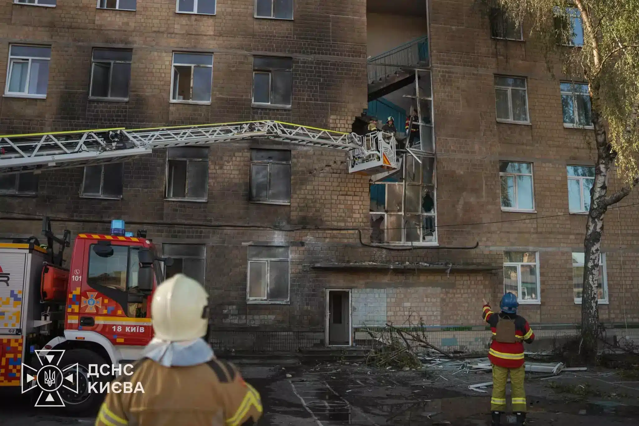 Рятувальники працюють біля пошкодженої частини цегляної будівлі з висувною драбиною пожежного автомобіля