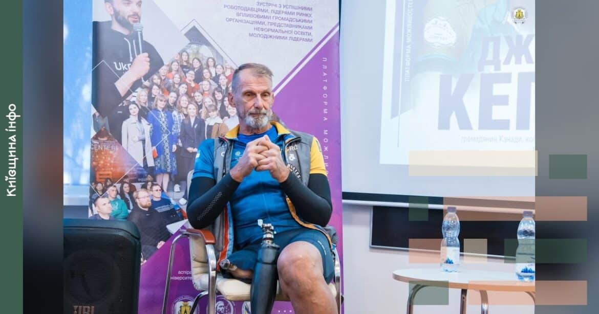 69-річний канадець у спортивному одязі з протезом на нозі сидить в аудиторії під час презентації про веломарафон Україною