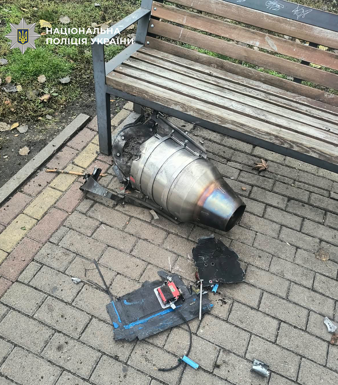 Уламки ворожого дрона з електронними деталями, покладені під лавку поруч з цегляною стіною