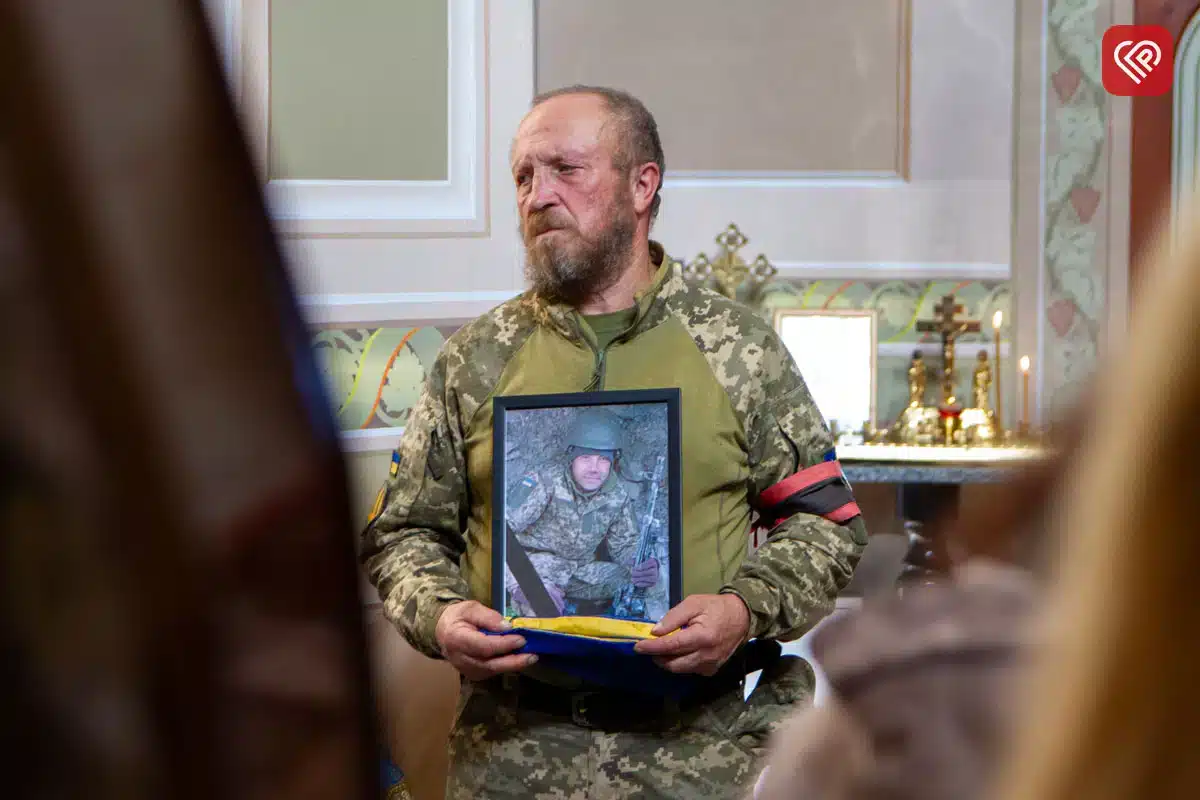 Військовослужбовець у камуфляжу тримає портрет загиблого побратима під час меморіальної церемонії
