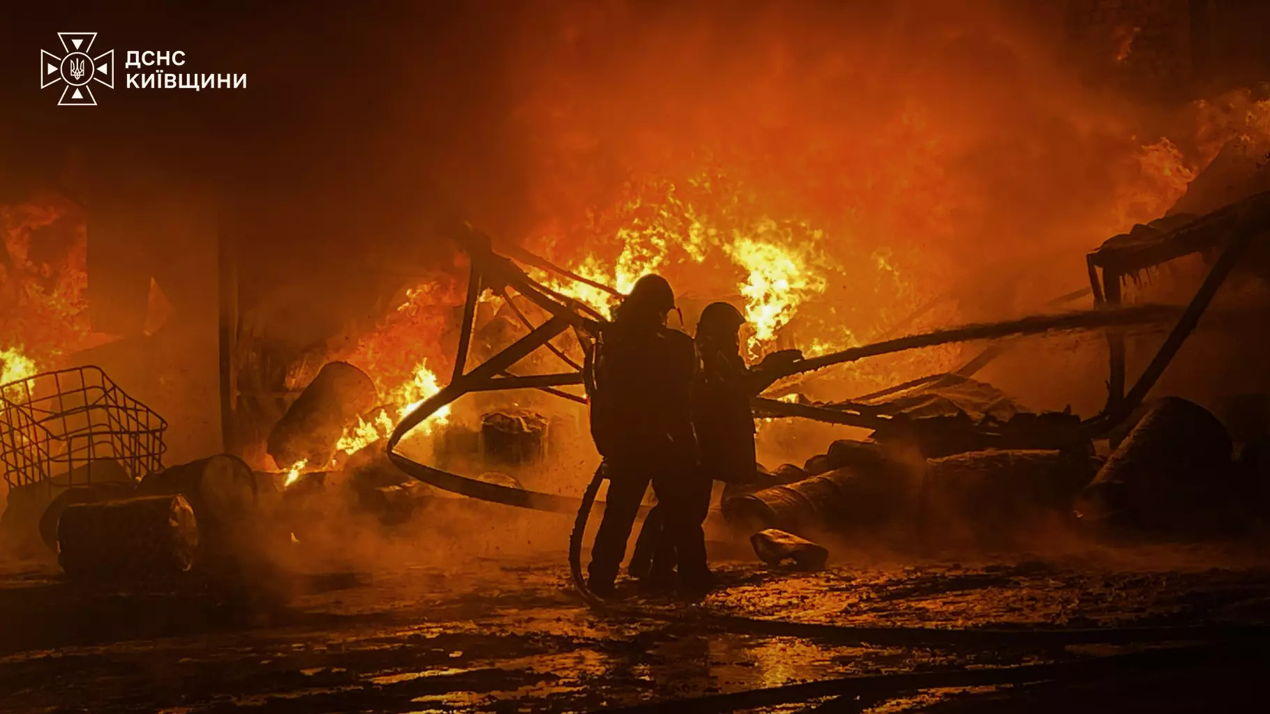 Двоє рятувальників гасять пожежу на промисловому підприємстві біля розрізаних металевих конструкцій