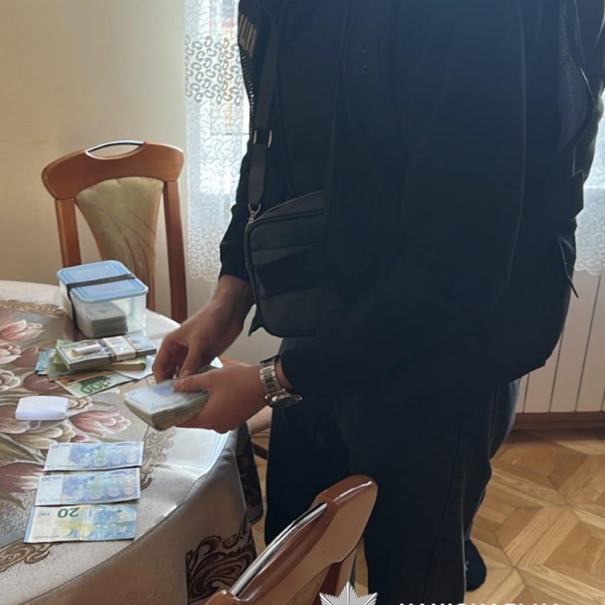 Правоохоронець перевіряє пачки грошей під час обшуку в приватному помешканні