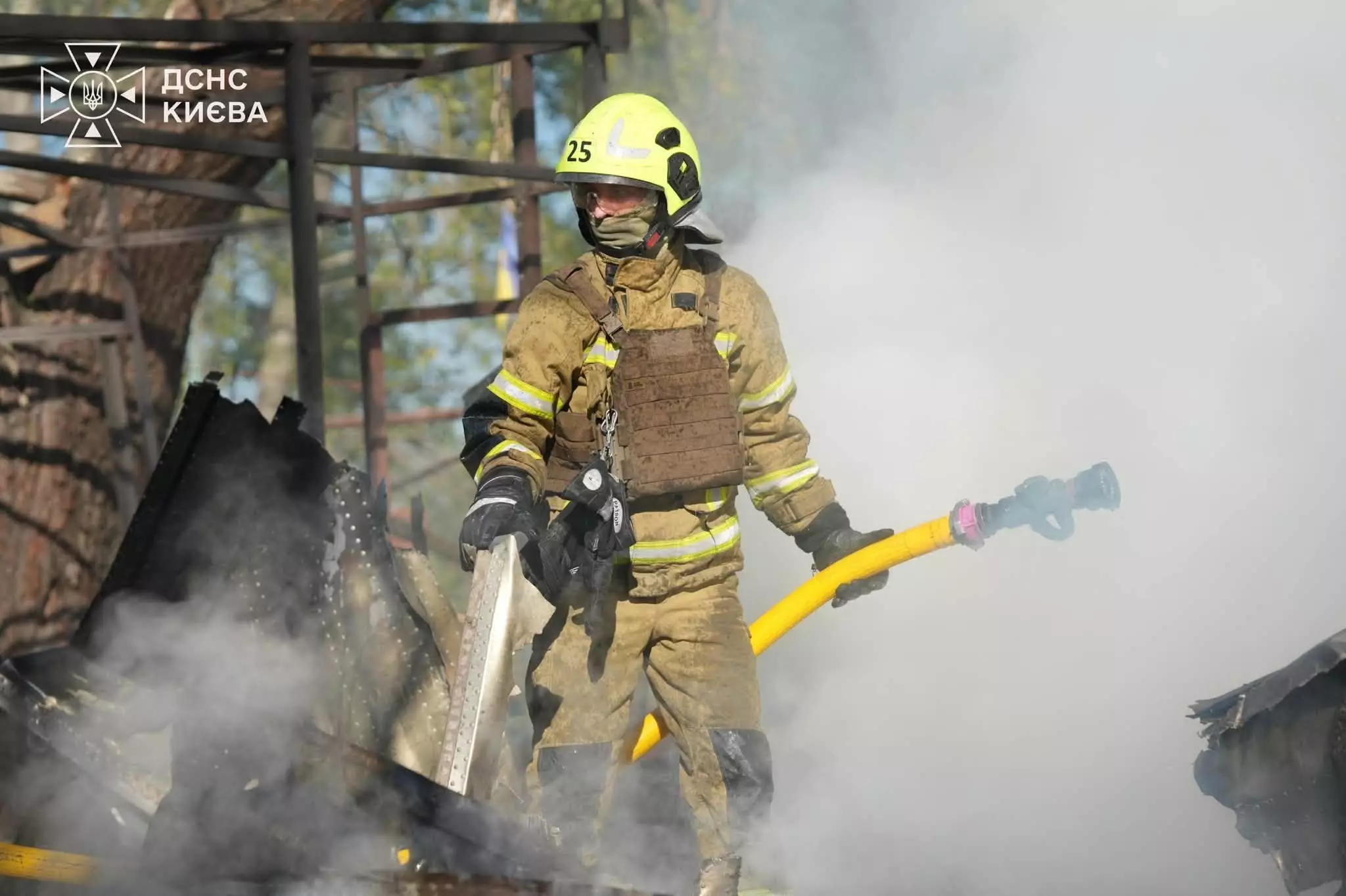 Рятувальник із пожежним шлангом гасить займання на деревʼяних конструкціях серед щільного диму
