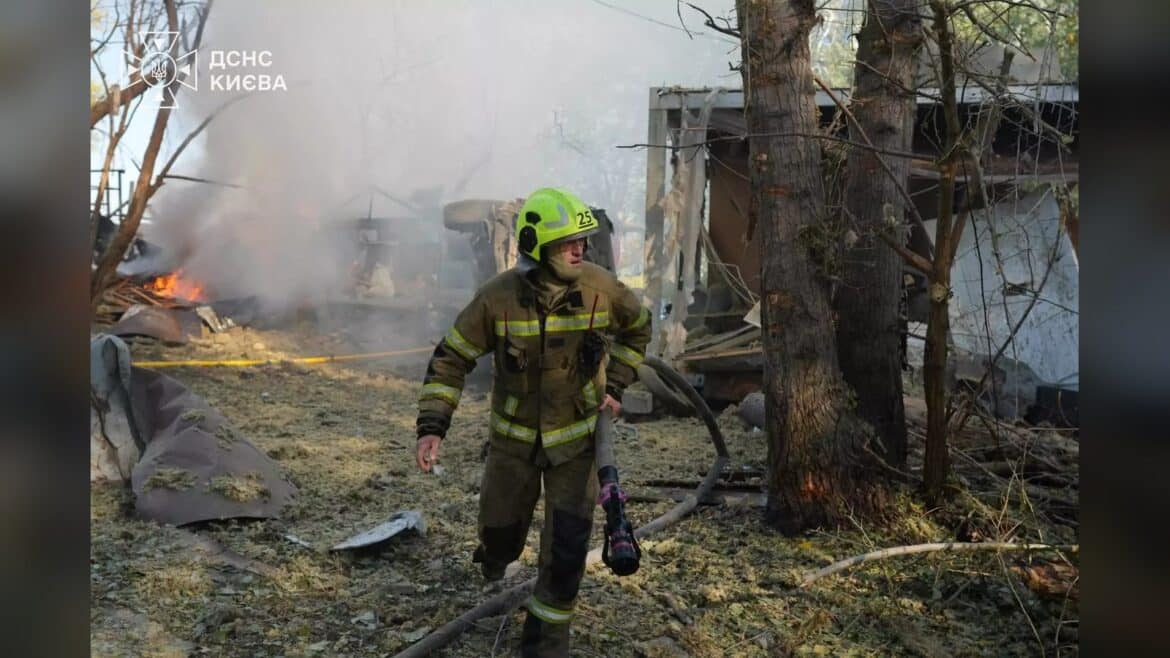 Рятувальник у жовтому касці та захисному одязі працює з пожежним шлангом серед диму та збитків від удару в Київі