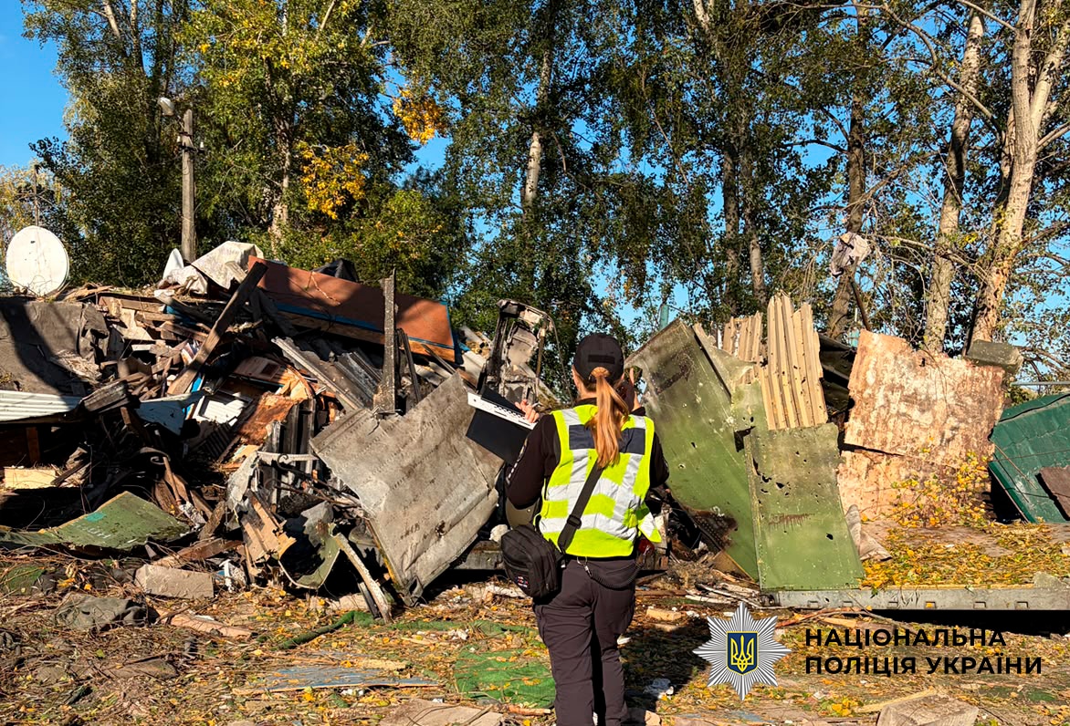 Поліцейський у жилеті документує пошкоджену техніку та обломки на місці обстрілу в Киї