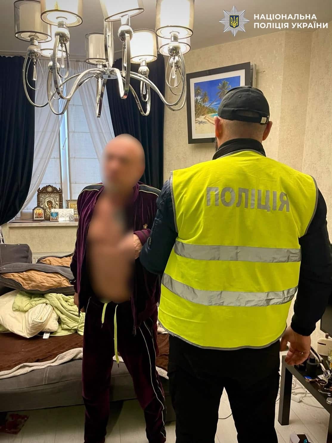 Поліцейський у жовтому жилеті спілкується з чоловіком у приватному житлі під люстрою