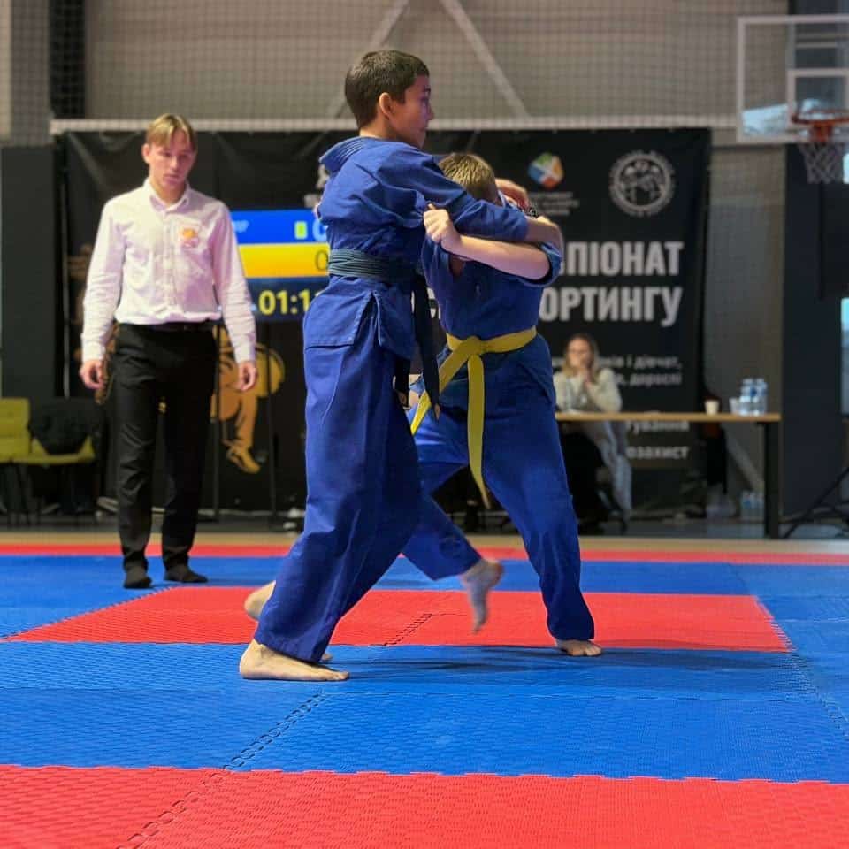 Спортсмен у синьому кімоно з жовтим поясом виконує кидок під час чемпіонату з хортингу