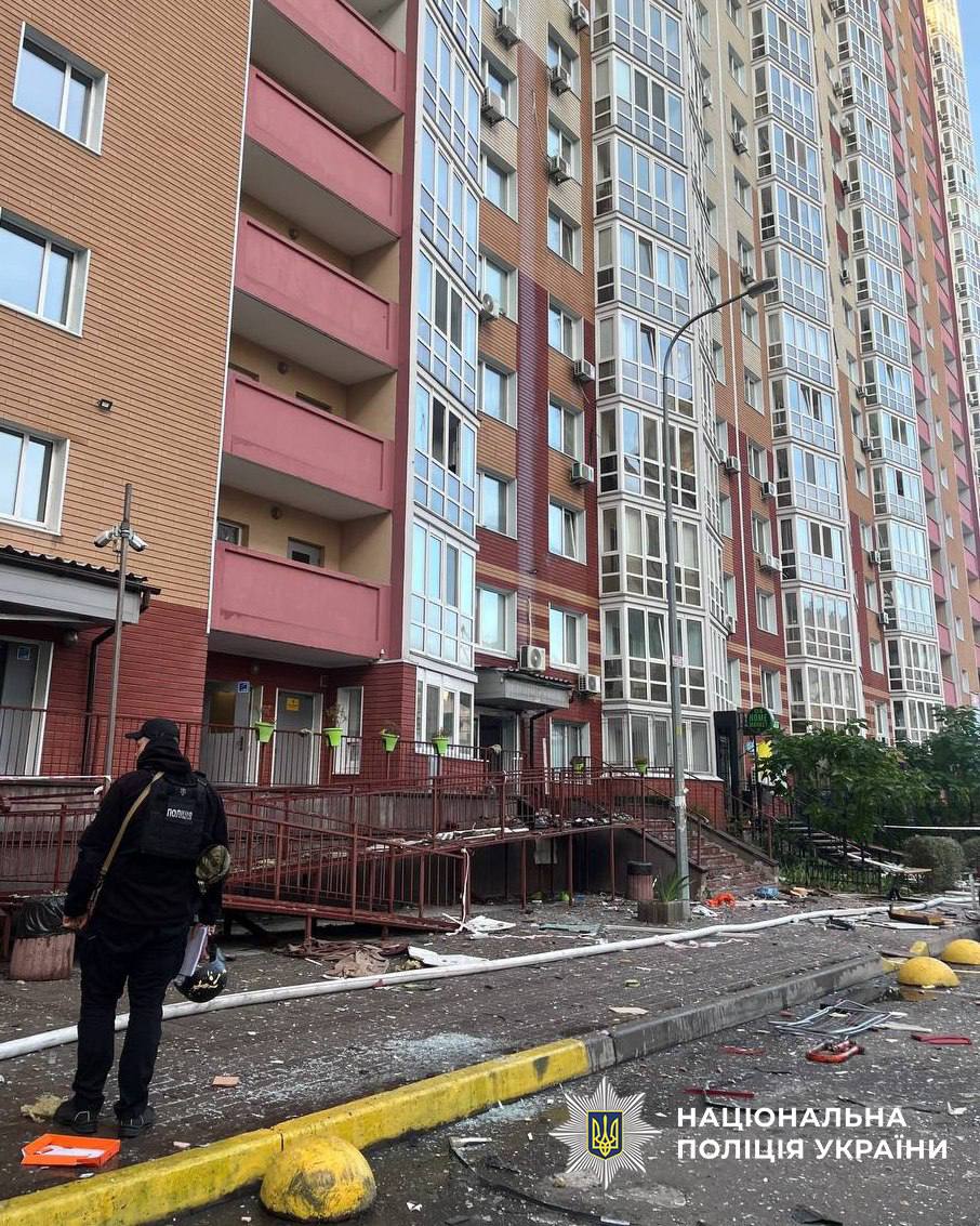 Поліцейський стоїть біля входу пошкодженої багатоповерхівки на Дарниці після атаки