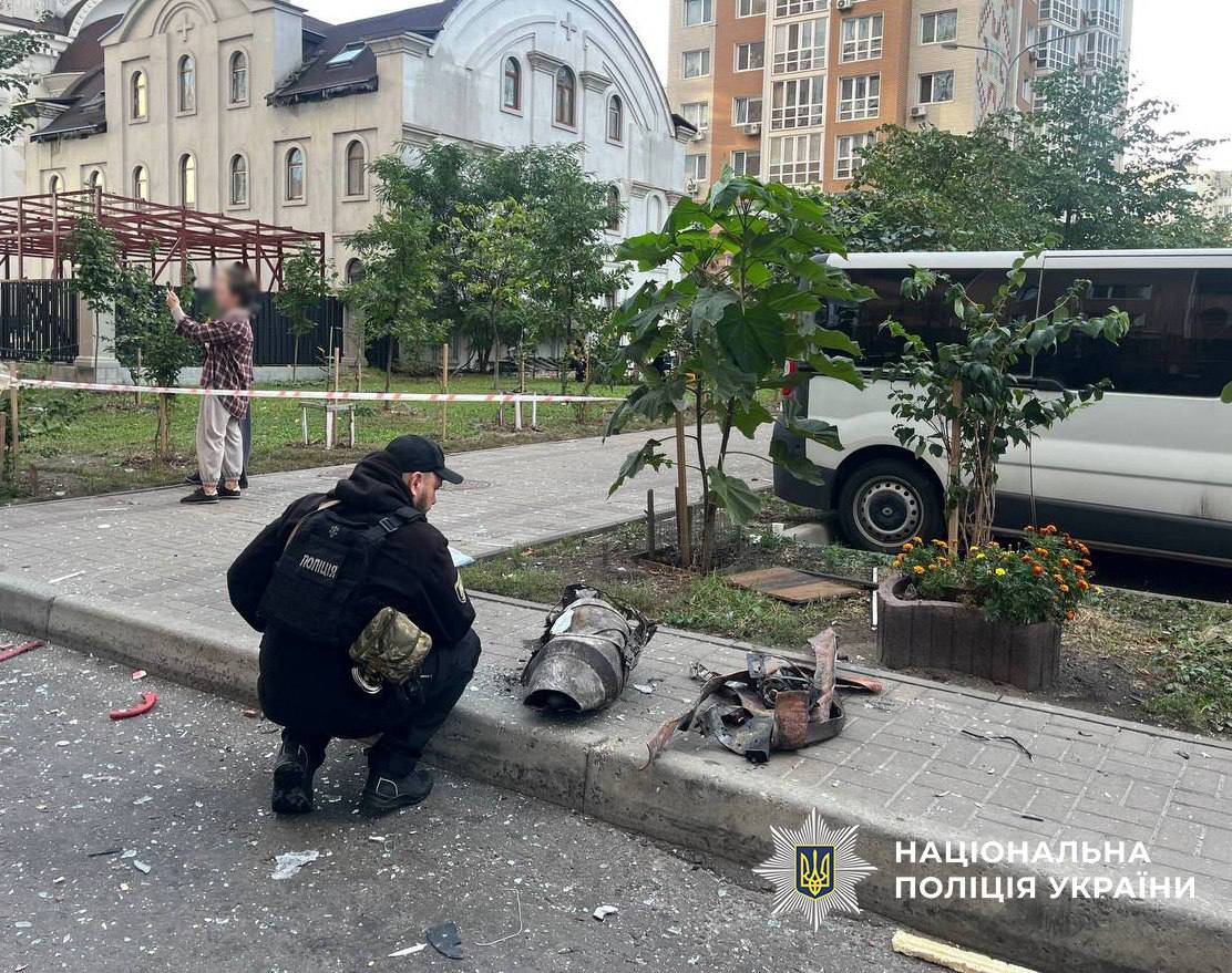 Поліцейський обстежує залишки боєприпасу на землі біля житлового будинку