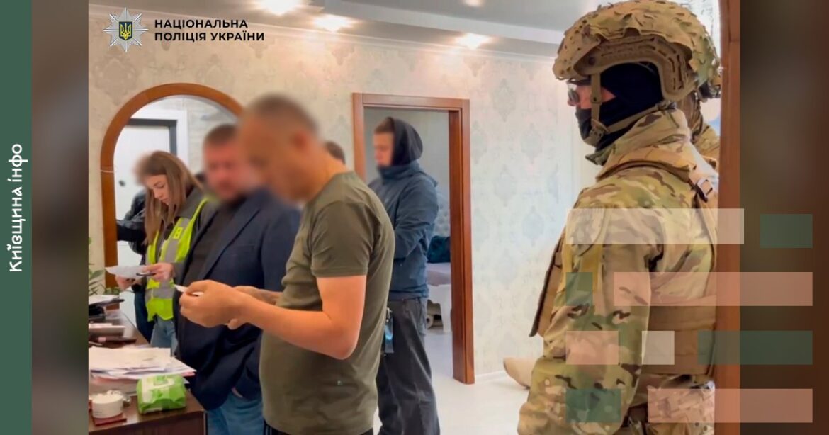 Поліцейський в камуфляжі спостерігає за групою людей в офісному приміщенні під час проведення спецоперації