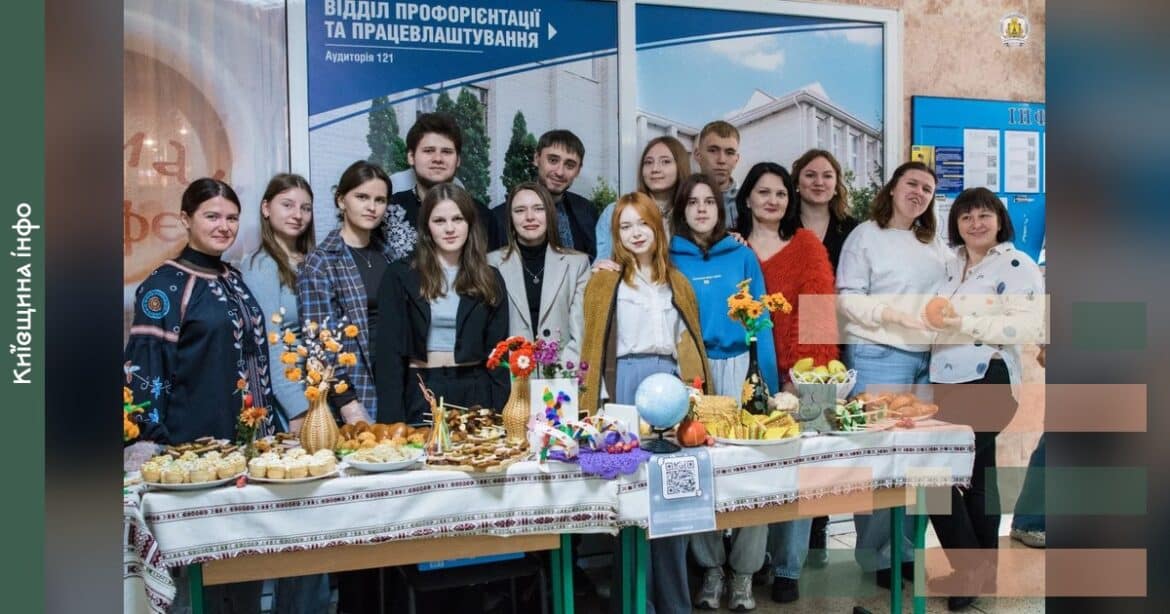 Студенти та викладачі університету стоять біля столу з українськими стравами на благодійному ярмарку