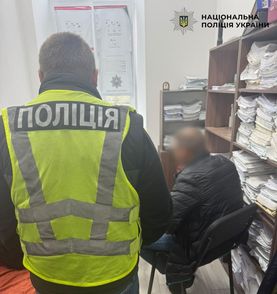 Поліцейський у жовтому жилеті з написом «ПОЛІЦІЯ» поруч із людиною в темній куртці в кабінеті з паперами