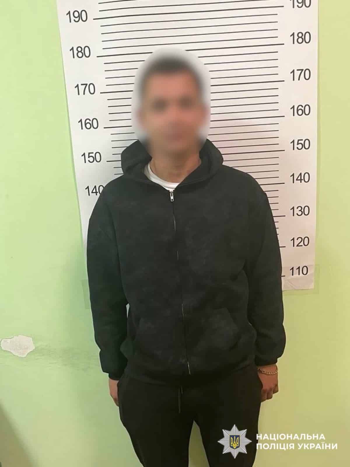 Чоловік у темному худі з розмитим обличчям стоїть перед ростоміром на зеленій стіні в приміщенні
