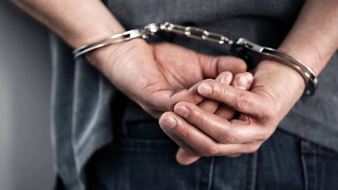 Руки людини в металевих наручниках за спиною, одягненої в сіру кофту та джинси