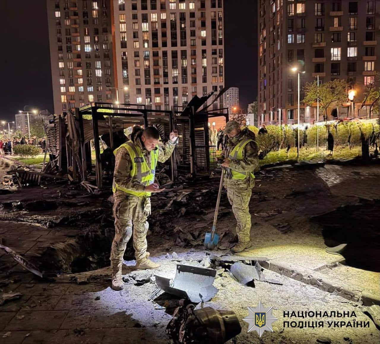Поліцейські обстежують уламки та руїни на місці попадання БпЛА в двір житлового комплексу вночі