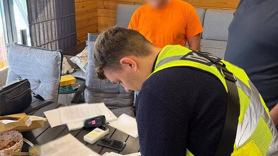 Поліцейський у жилеті в'яжеться з документами під час розслідування схеми розтрати бюджету на ремонті доріг