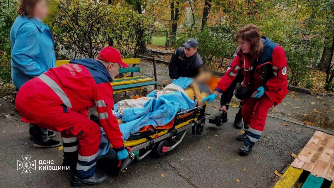Рятувальники в червоних костюмах і медичні працівники транспортують чоловіка на жовто-синьому носилку до машини швидкої
