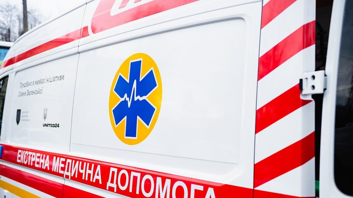 Бік машини швидкої допомоги з написом «Екстрена медична допомога» та синім знаком медицини на жовтому колі