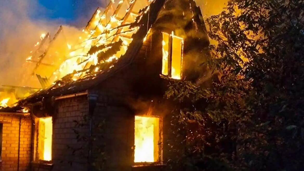 Житловий будинок у вогні вночі: полум'я пробиває дах і вікна цегляної будівлі