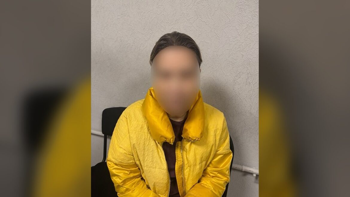 Жінка з розмитим обличчям у жовтій стьобаній куртці сидить на чорному стільці біля світлої стіни