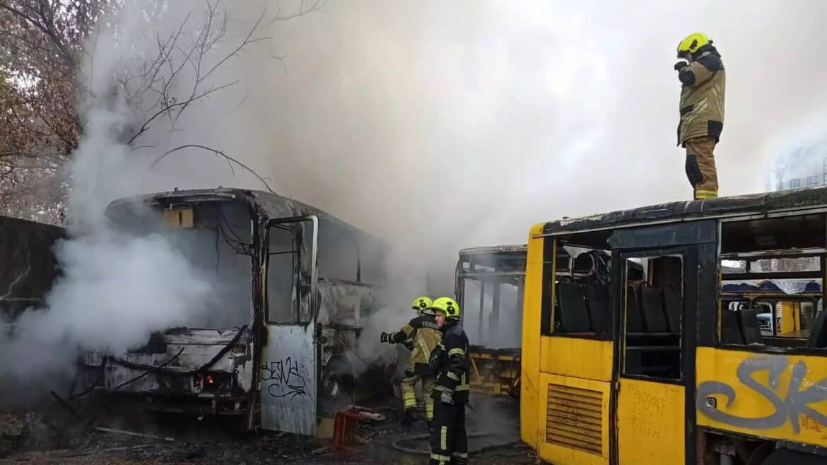 Пожежники гасять обгорілі автобуси на парковці, над ними стелиться густий дим, на даху стоїть рятувальник